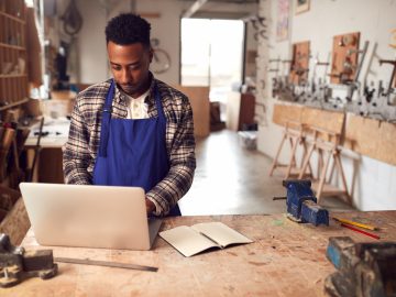 Male Craftsman In Carpentry Workshop For Bamboo Bicycles  Doing Accounts On Laptop